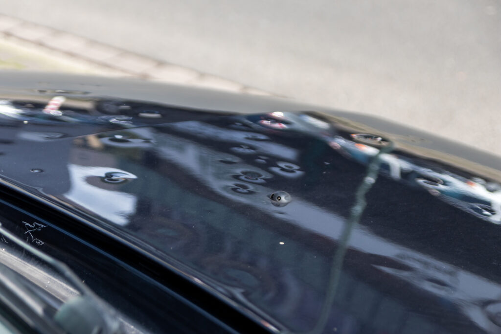 Car engine hood with many hail damage dents show the forces of nature and the importance of car insurance and a replacement value insurance against stormy weather and storm hazards or extreme weather